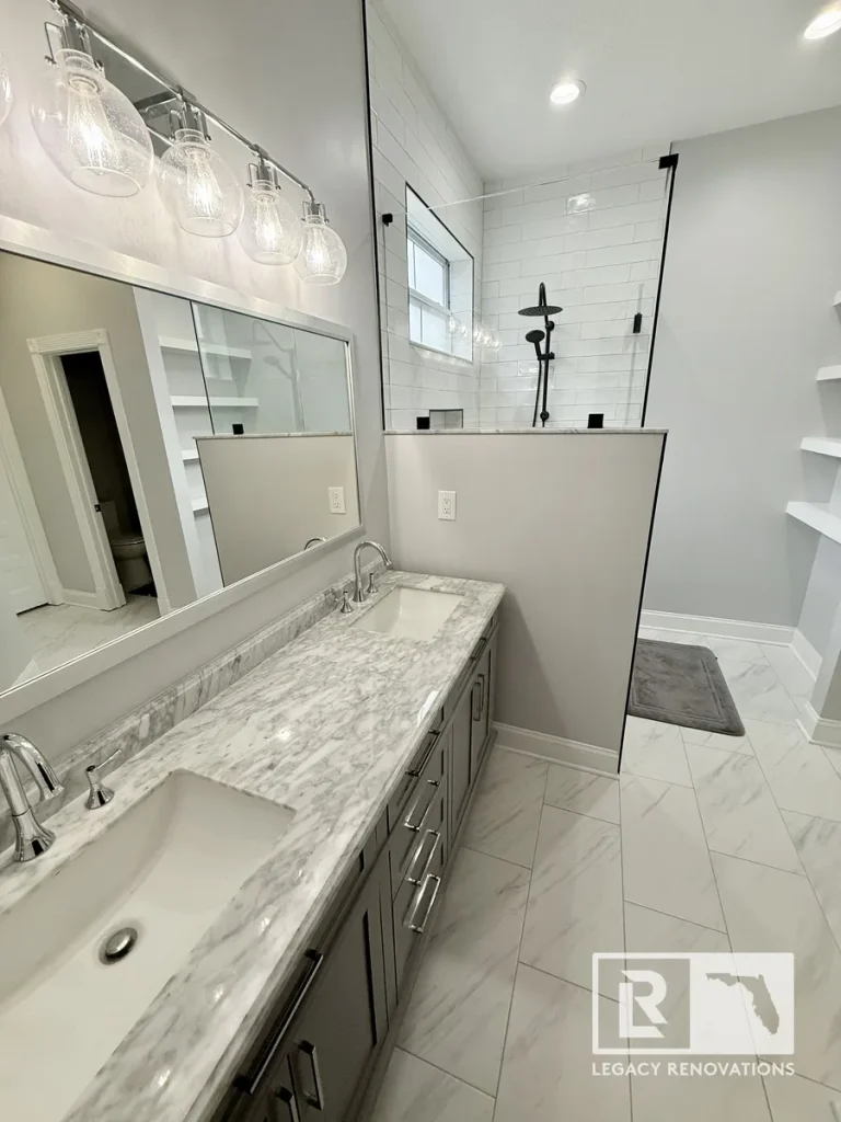 Modern bathroom featuring a double gray vanity with a marble countertop, frameless glass shower, and white subway tile.