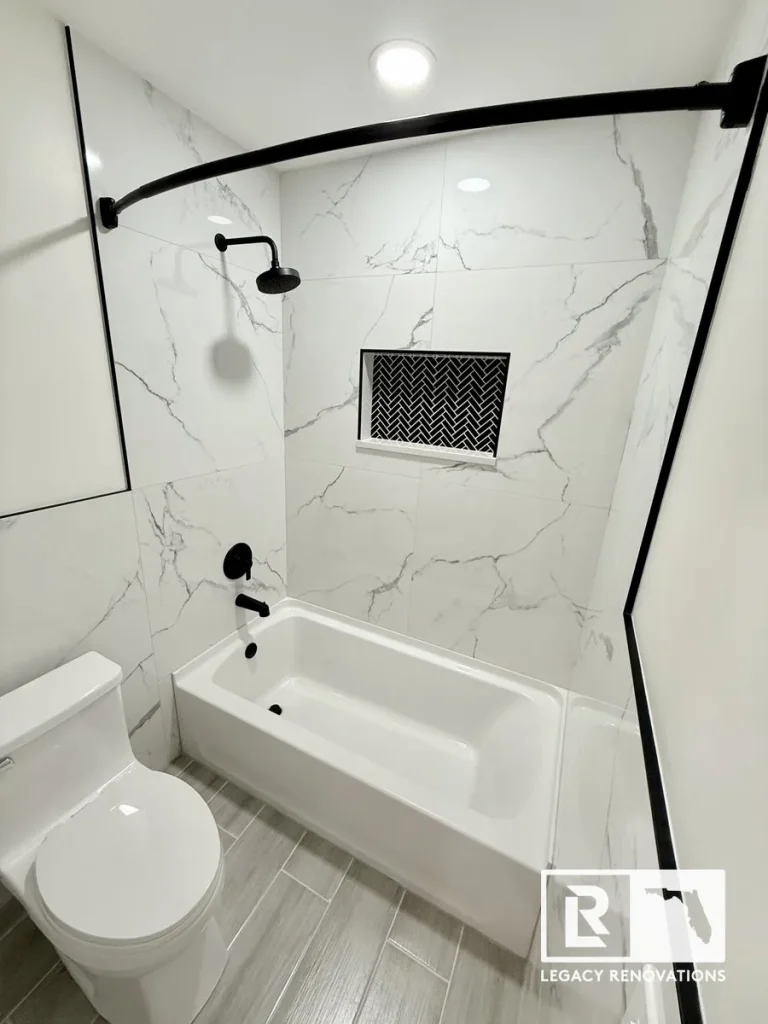 Modern bathtub shower remodel featuring large-format marble-look wall tile, black shower fixtures, a curved shower rod, and a recessed herringbone tile niche.