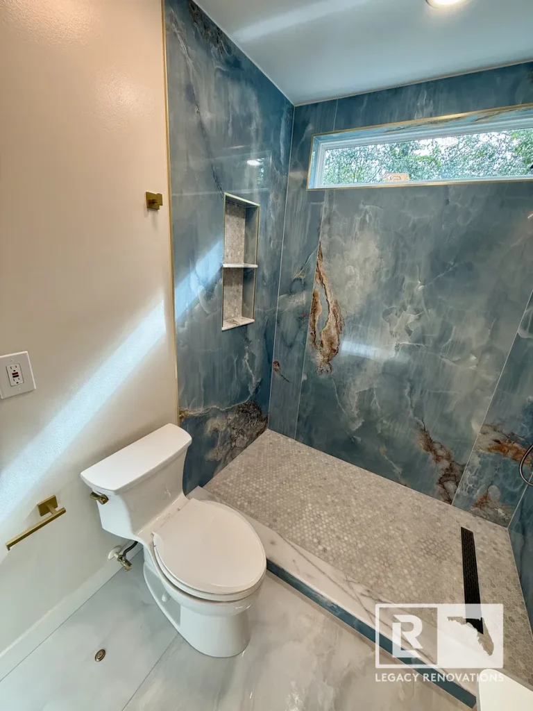 Modern walk-in shower with large-format porcelain slab walls, recessed niche, mosaic tile floor, and brushed brass fixtures in Jacksonville, FL