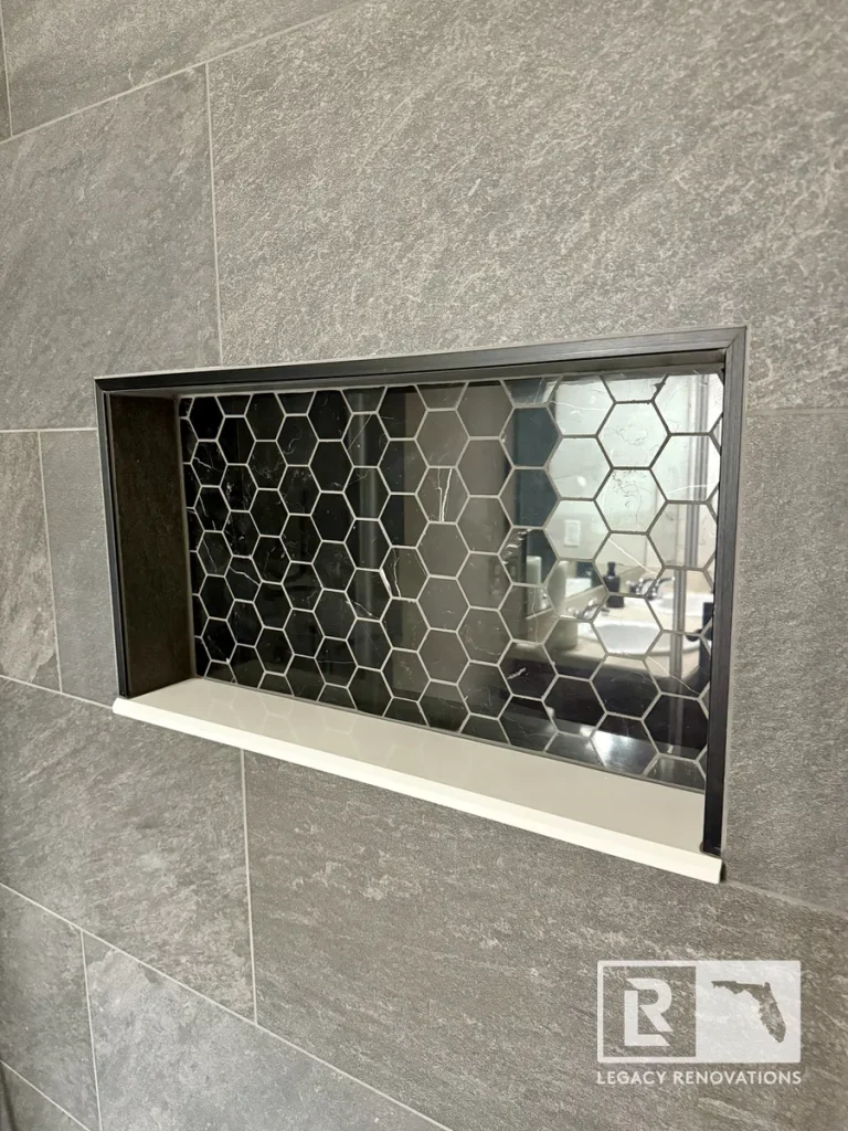 Recessed shower niche featuring black hexagon accent tile, gray porcelain wall tile, and a solid surface shelf in a remodeled bathroom.