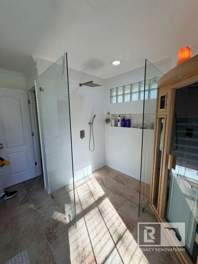 Frameless glass walk-in shower with textured white wall tile, recessed niche, glass block window, matte black rain shower, and porcelain floor tile in a Jacksonville, FL bathroom remodel.