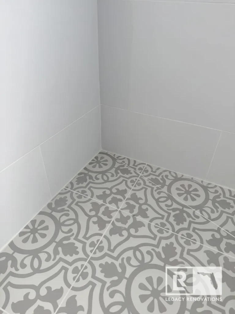 Close-up of gray patterned porcelain shower floor tile with large-format light gray wall tile in a bathroom remodel in Jacksonville, FL.