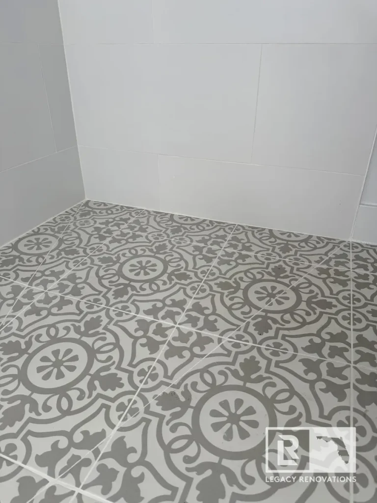Grey and white patterned mosaic tile shower floor meeting white large-format wall tiles in a Jacksonville, FL bathroom renovation.