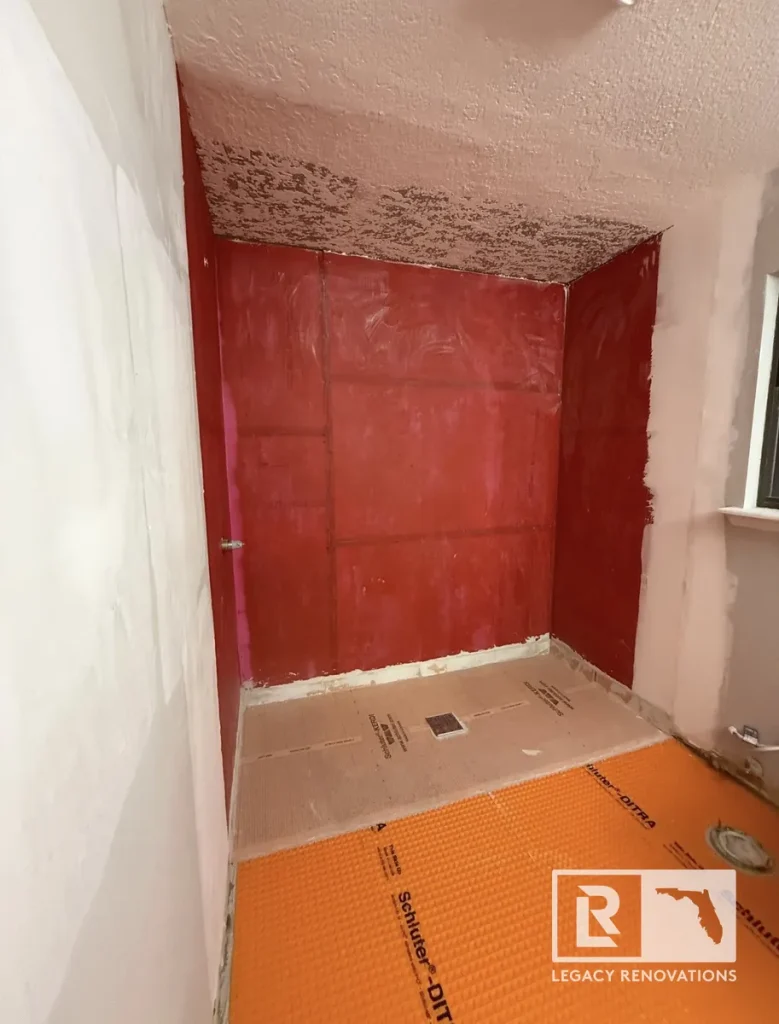 Walk-in shower enclosure prep in Jacksonville, FL with red liquid wall waterproofing membrane, Schluter-KERDI shower pan, and Schluter-DITRA floor membrane.