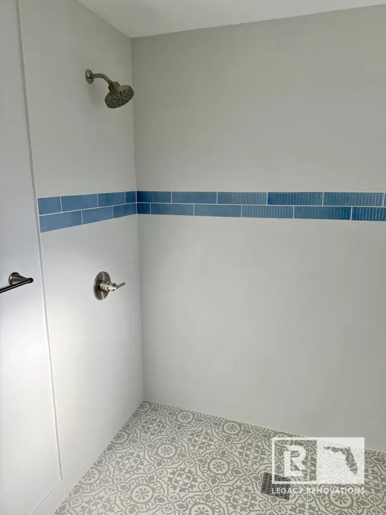 Completed walk-in shower in Jacksonville, FL featuring white wall tile, a blue mosaic accent band, patterned floor tile, and brushed nickel fixtures.