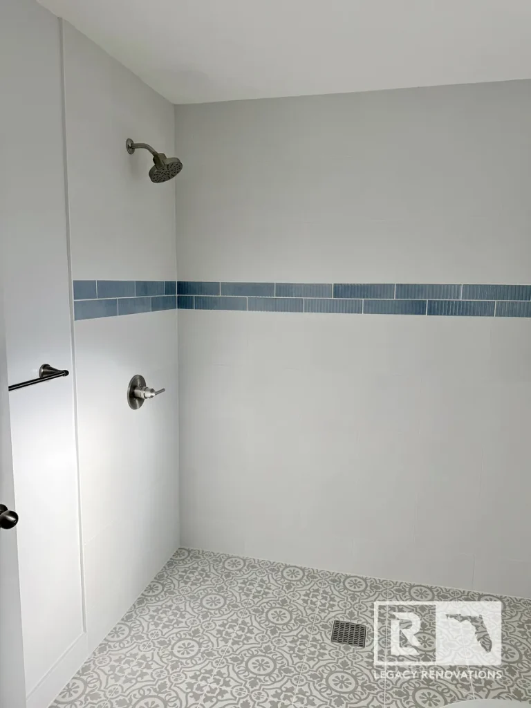 Modern walk-in shower with large-format wall tile, blue accent tile, patterned porcelain floor, and brushed nickel shower fixtures in Jacksonville, FL.