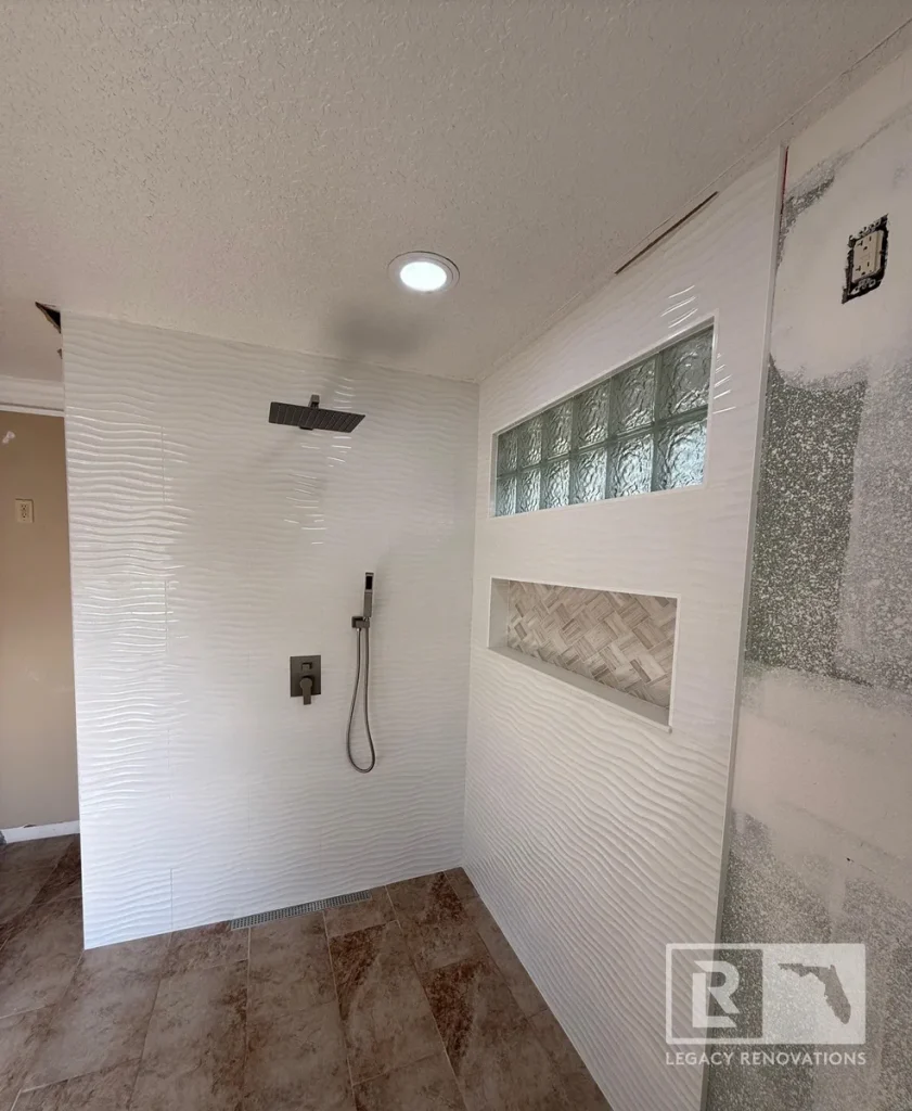 Walk-in shower with white wave wall tile, glass block window, recessed shower niche, matte black rain shower fixture, and large-format floor tile in Jacksonville, FL.