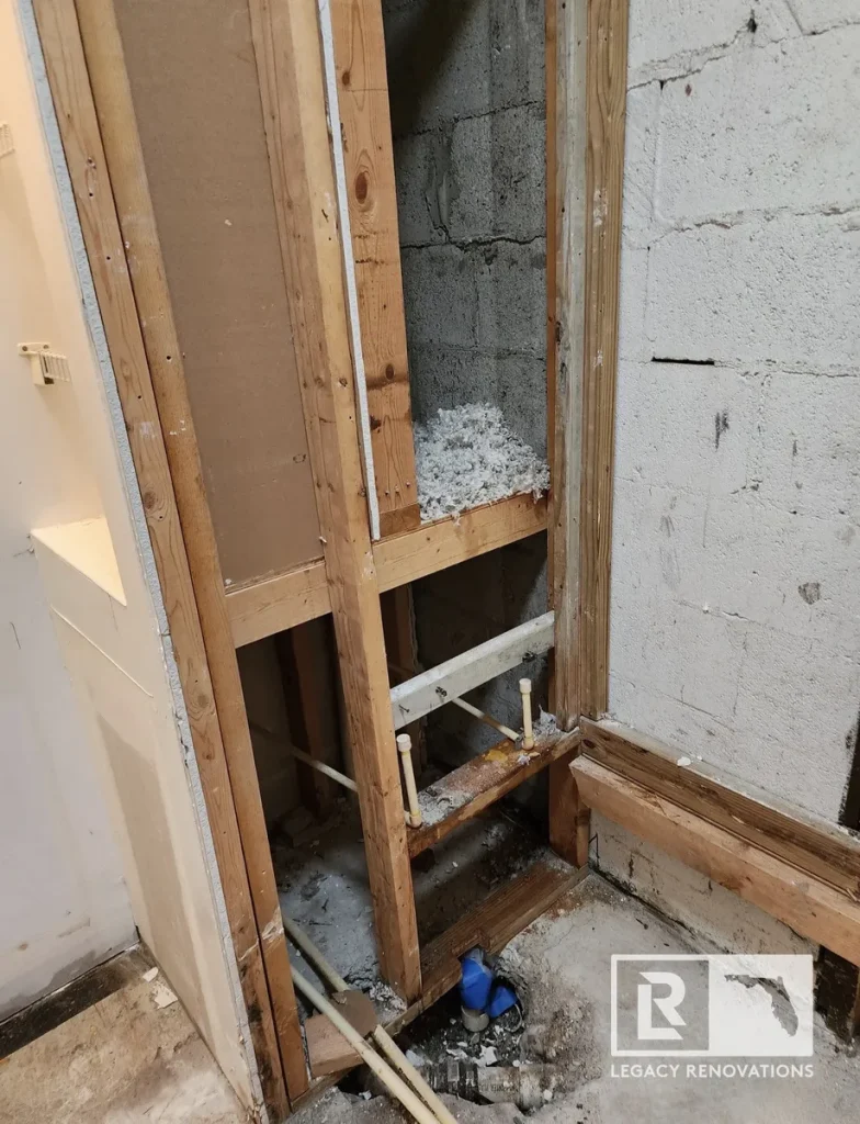 Exposed wall framing, concrete block walls, insulation, and new plumbing pipes during the demolition phase of a bathroom remodel by Legacy Renovations in Jacksonville, FL.