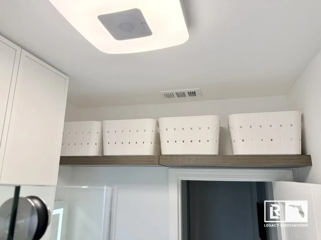 A finished bathroom interior featuring a high floating shelf with four white woven plastic storage baskets, bright ceiling lighting, and crisp white walls by Legacy Renovations in Jacksonville, FL.