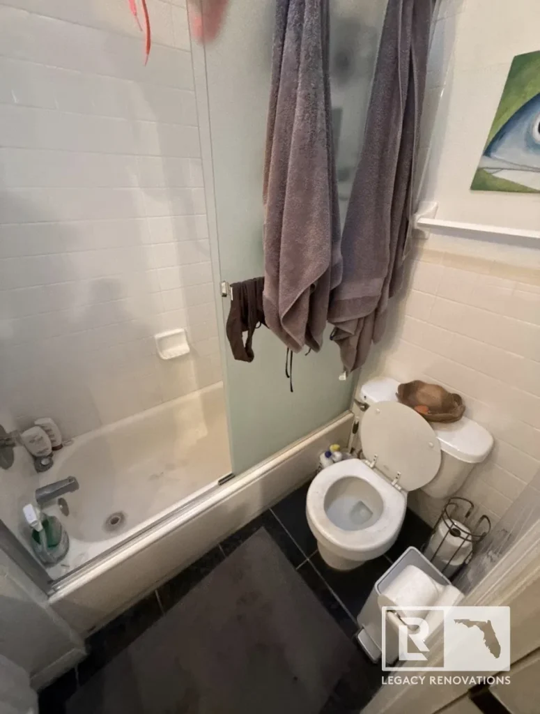 Before bathroom remodel with a bathtub, sliding glass shower doors, white tile walls, and compact layout in Jacksonville, FL.