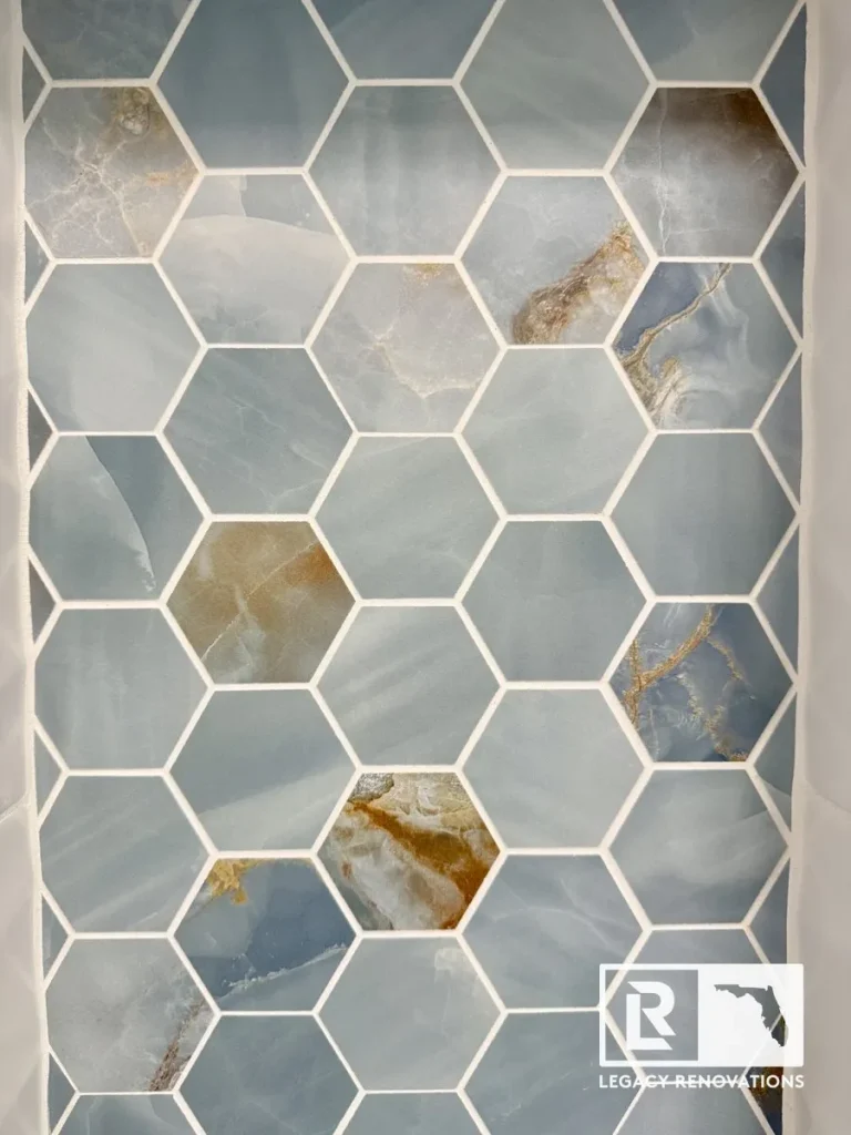 A detailed close-up of installed blue onyx-look hexagon mosaic wall tiles featuring white grout lines and natural gold and amber veining by Legacy Renovations in Jacksonville, FL.