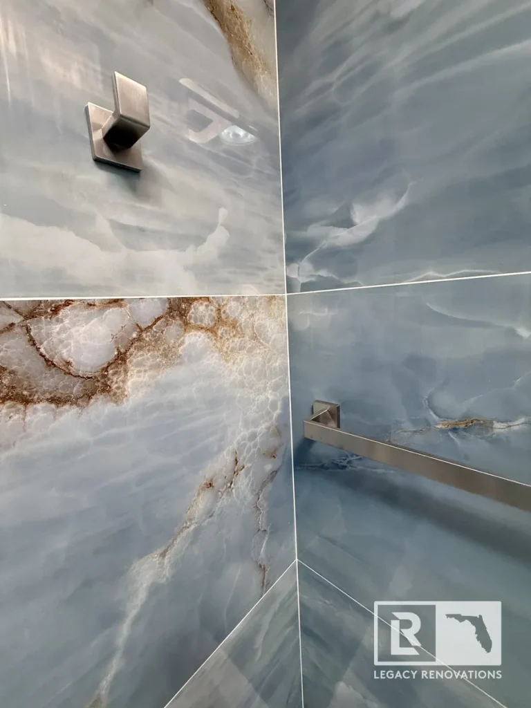 Close-up of blue porcelain shower wall tile with brushed nickel towel bar and robe hook during a custom bathroom remodel in Jacksonville, FL.