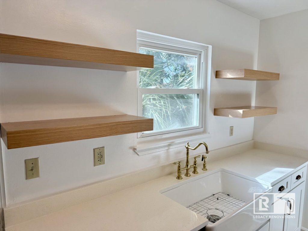 Custom kitchen with floating wood shelves, farmhouse utility sink, brushed brass faucet, white quartz countertops, and white shaker cabinets in Jacksonville, FL.