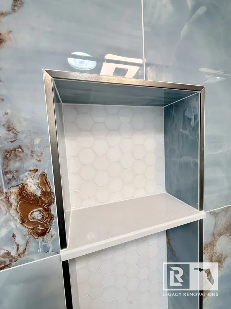 Custom recessed shower niche with white hexagon tile, quartz shelf, and blue porcelain shower wall tile in a luxury bathroom remodel in Jacksonville, FL.