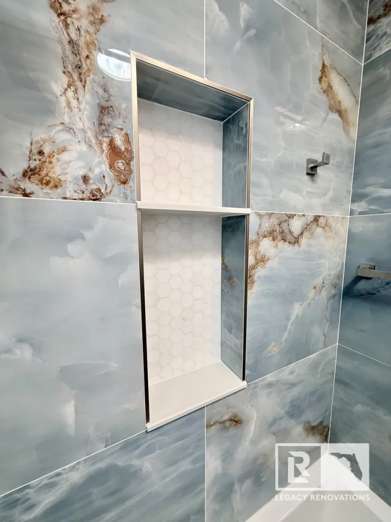 Double recessed shower niche with white hexagon mosaic tile, quartz shelves, brushed nickel trim, and blue porcelain wall tile in a custom bathroom remodel in Jacksonville, FL.
