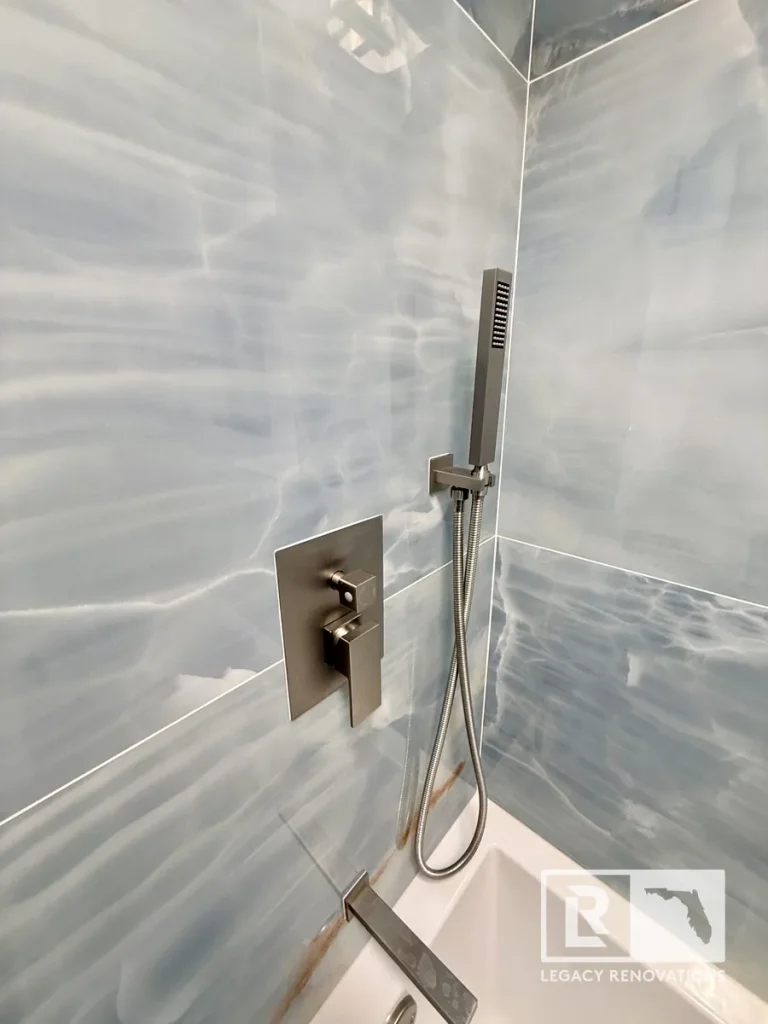 Modern bathroom shower with blue porcelain tile walls, brushed nickel handheld shower fixture, and contemporary shower valve installed during a bathroom remodel in Jacksonville, FL.