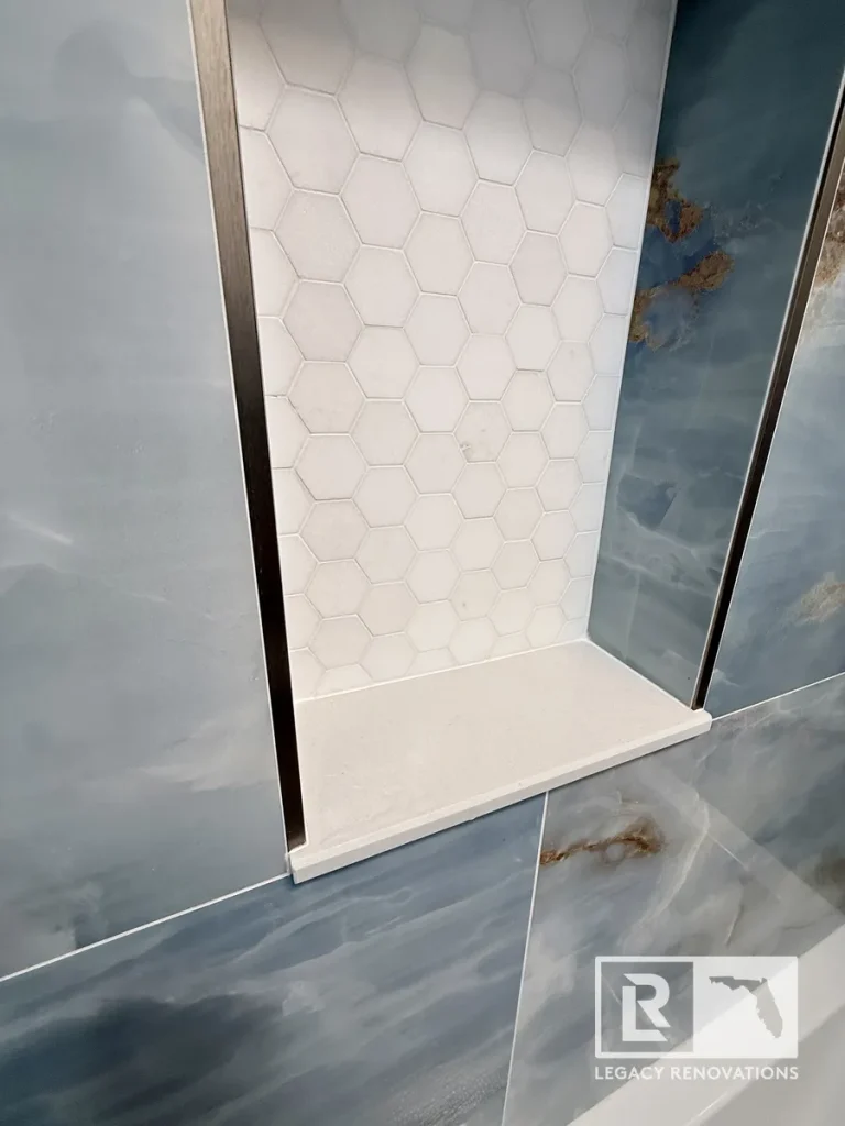 Close-up of a custom shower niche with white hexagon mosaic tile, quartz shelf, and polished blue porcelain wall tile in a Jacksonville, FL bathroom remodel.