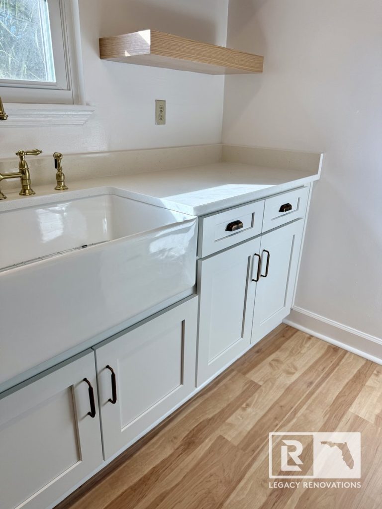 Bright kitchen renovation in Jacksonville, FL featuring custom white recessed panel cupboards, a white apron-front sink, quartz countertops, and brass fixtures.