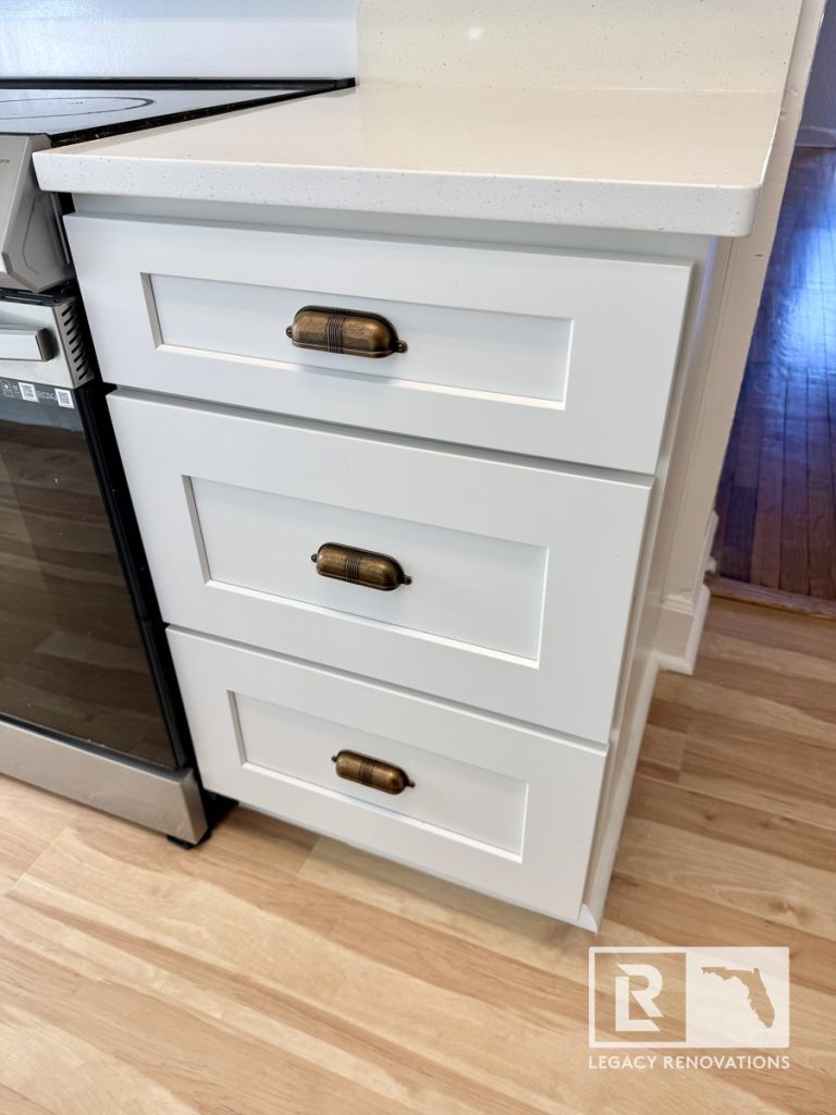 Close-up of custom white shaker cabinet drawers with antique brass cup pulls and white quartz countertop in a Jacksonville, FL home remodel.