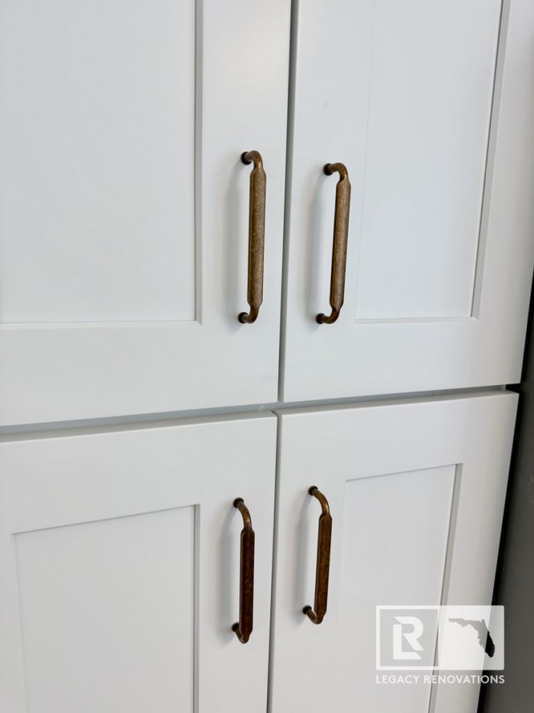 Close-up of modern white shaker cabinet doors with antique brass pull handles installed during a kitchen renovation in Jacksonville, FL.