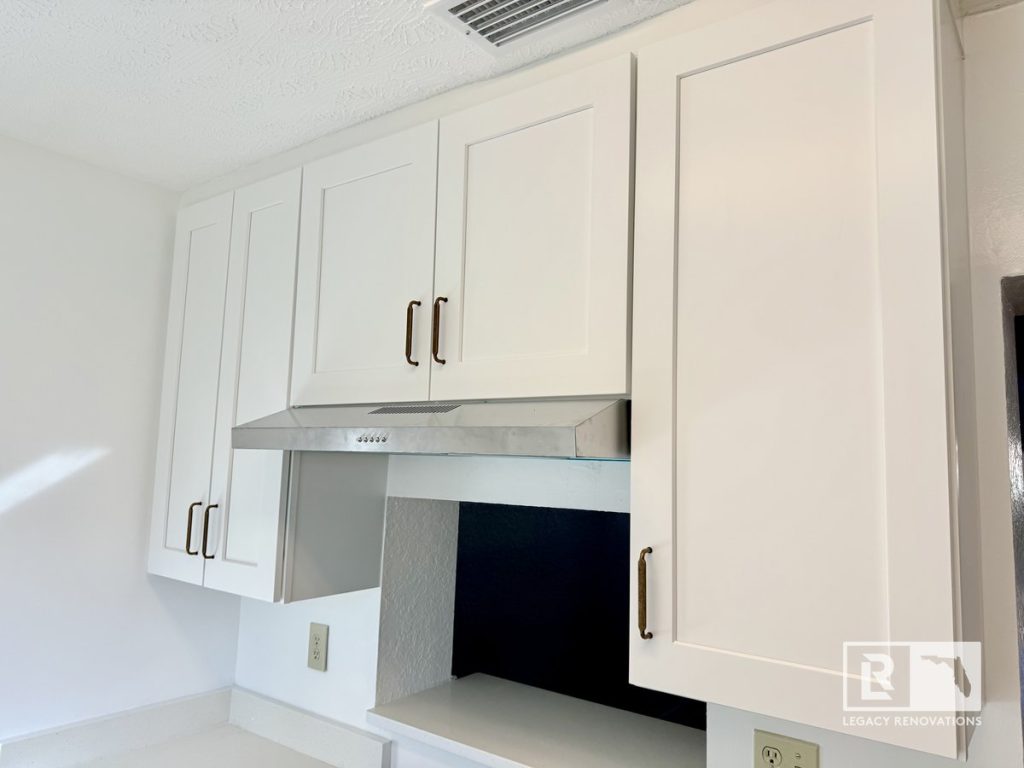 Custom white shaker kitchen wall cabinets with stainless steel range hood, quartz countertops, and antique brass cabinet handles in a Jacksonville, FL kitchen remodel.