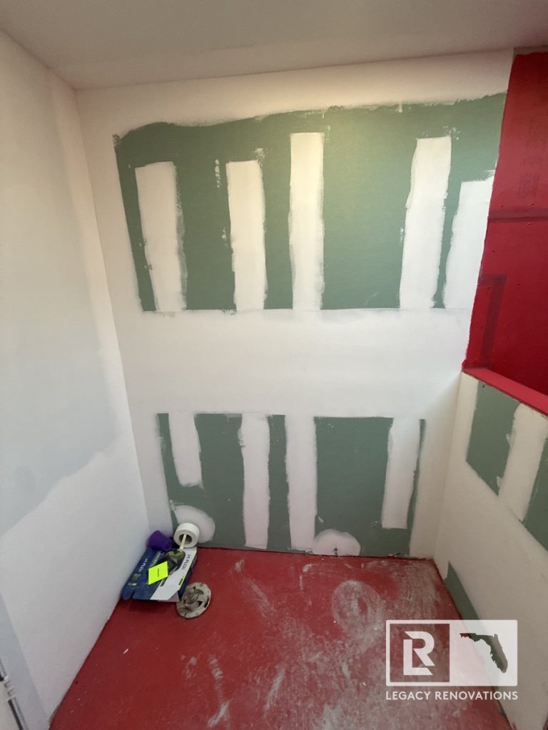 A bathroom renovation in progress featuring moisture-resistant green drywall with taped seams and a red waterproofed subfloor layer by Legacy Renovations in Jacksonville, FL.