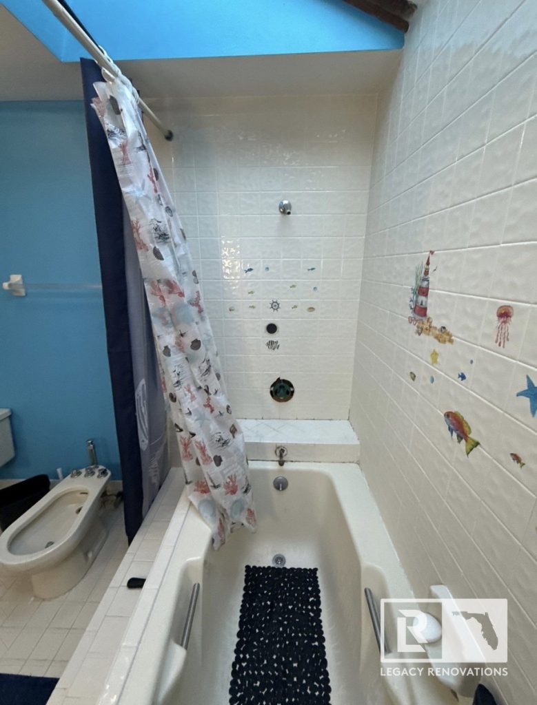 An outdated bathroom before renovation showing a beige drop-in bathtub, ocean themed wall tiles, a bidet, and a skylight by Legacy Renovations in Jacksonville, FL.