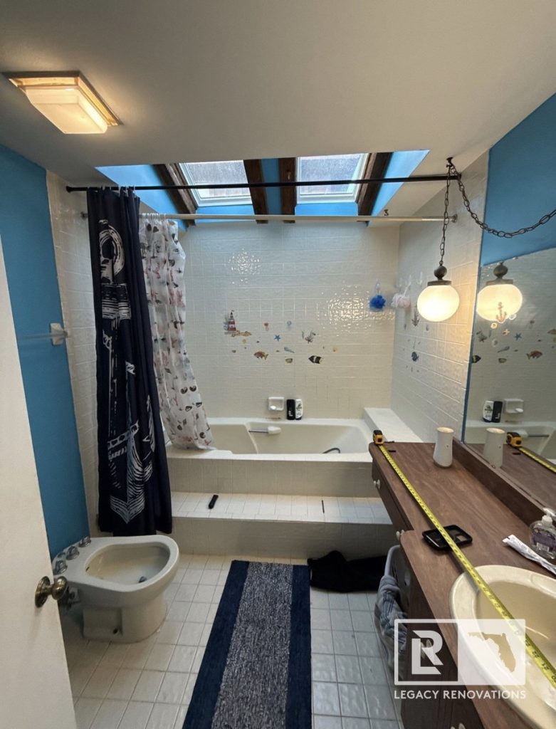 An outdated master bathroom prior to remodel featuring a step-up bathtub, bidet, wood vanity with yellow measuring tape, and overhead skylights by Legacy Renovations in Jacksonville, FL.