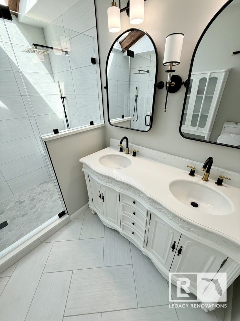 Complete master bathroom remodel in Jacksonville, FL, featuring an ornate white double vanity, black arched mirrors, and a glass walk-in shower with a skylight by Legacy Renovations.