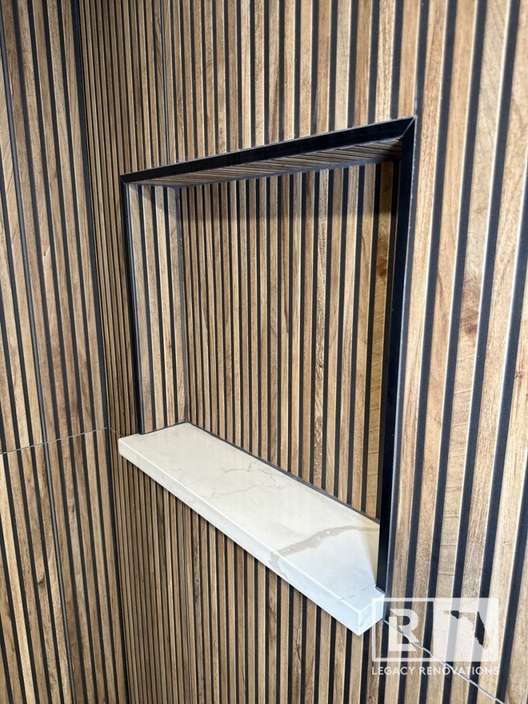 Recessed shower niche with fluted wood-look tile, black trim, and a white quartz shelf in a bathroom remodel in Costa Verde, Jacksonville, FL.