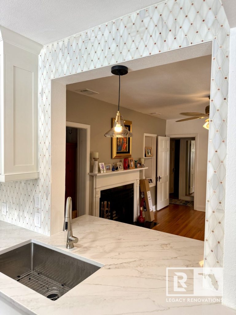 Kitchen remodel in Jacksonville, FL featuring quartz countertops, a stainless steel farmhouse sink, geometric tile backsplash, a pass-through opening, and modern pendant lighting.
