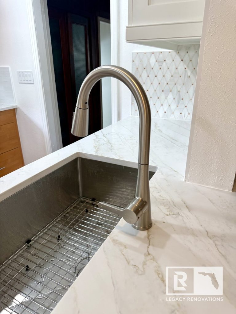Kitchen remodel in Jacksonville, FL featuring a stainless steel pull-down faucet, undermount farmhouse sink, quartz countertops, and a geometric tile backsplash.