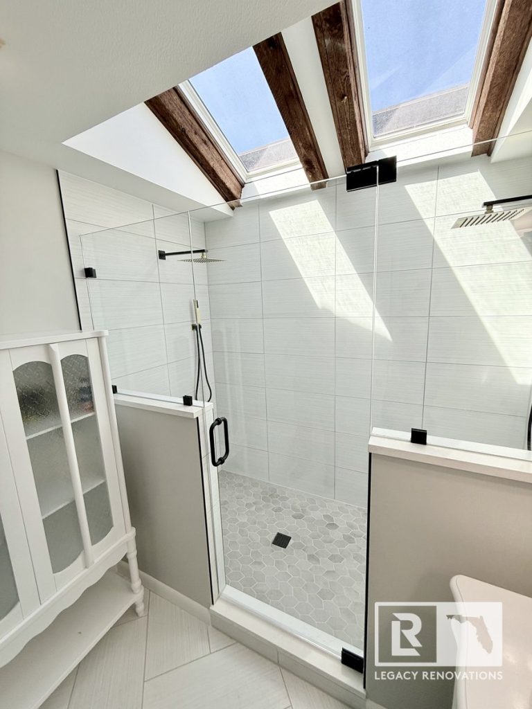 Custom walk-in glass shower with dual skylights, rustic wood beams, matte black hardware, and hexagon tile floor by Legacy Renovations in Jacksonville, FL.