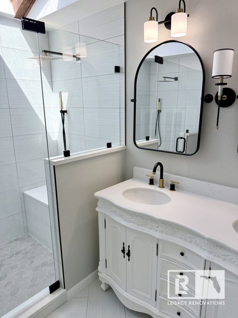 Complete master bathroom remodel in Jacksonville, FL featuring an ornate white vanity, arched mirror, and a frameless glass walk-in shower with hexagon tile floor.