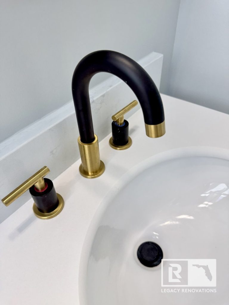 Close-up of a matte black and brushed gold dual-handle faucet on a white quartz vanity by Legacy Renovations in Jacksonville, FL.