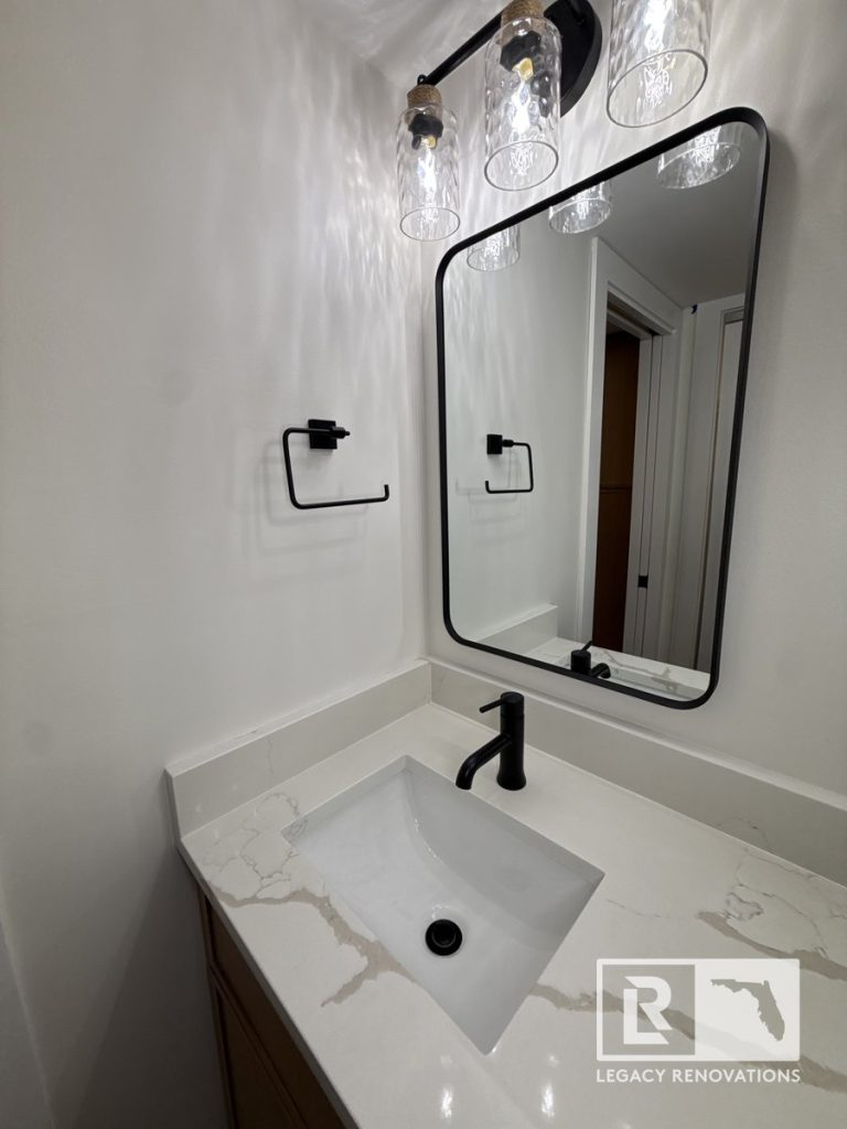 Modern bathroom vanity with white quartz countertops, matte black faucet, rounded mirror, and seeded glass light fixtures in Jacksonville, FL