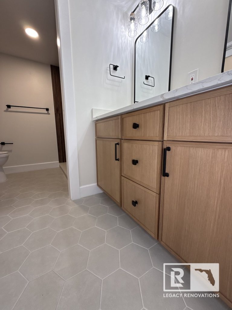Modern bathroom remodel featuring custom light oak vanity cabinets, grey hexagon tile floor, and matte black fixtures in Jacksonville, FL