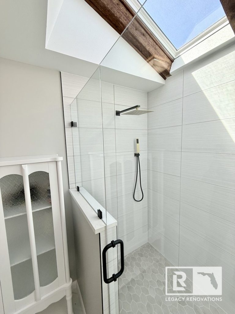 Modern walk-in shower with a large skylight, white textured wall tiles, grey hexagon floor tiles, and matte black fixtures by Legacy Renovations in Jacksonville, FL.