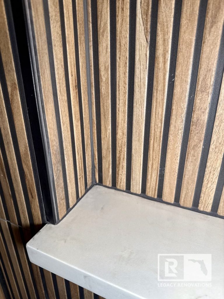 Close-up of a white quartz shower shelf with matte black trim and fluted wood-look tile in a bathroom remodel in Jacksonville, FL.