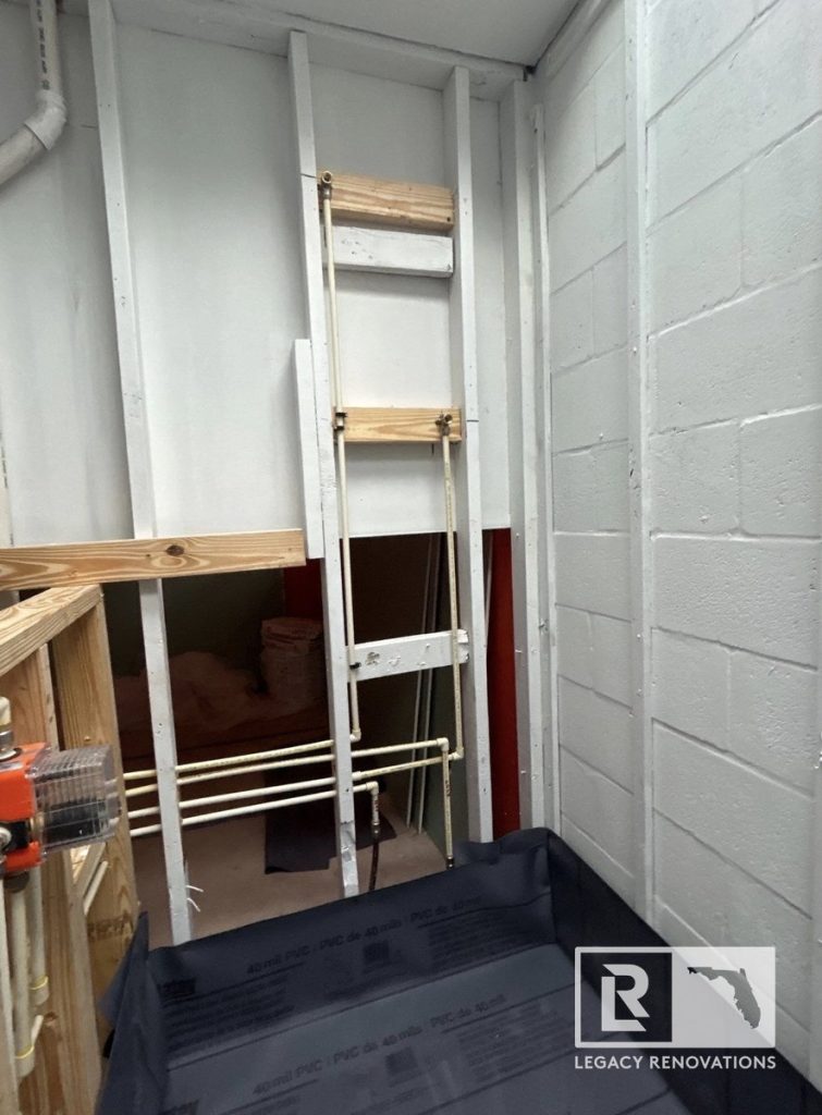 A bathroom renovation during the framing stage showing a black PVC shower pan liner, open wall studs, and rough plumbing lines by Legacy Renovations in Jacksonville, FL.
