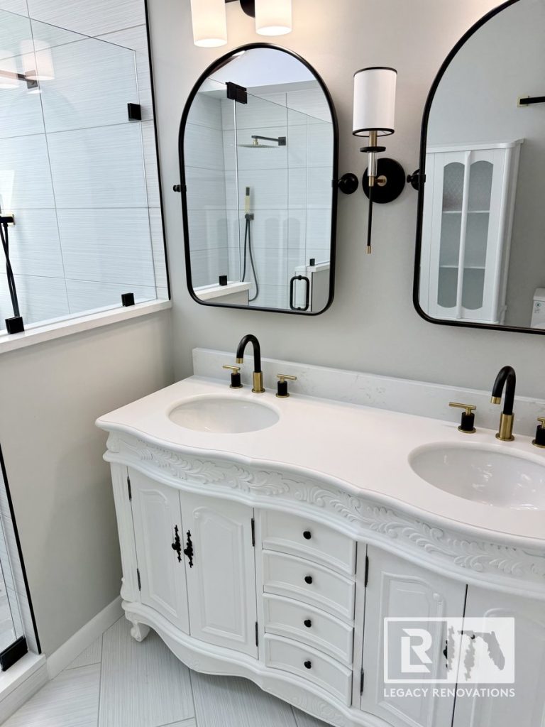 Ornate white double vanity with quartz countertops, black arched mirrors, and matte black and gold faucets in a Jacksonville, FL bathroom renovation by Legacy Renovations.