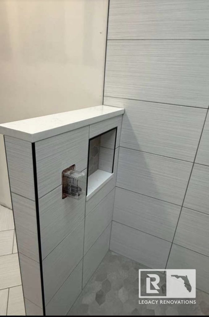 Tiled shower half wall topped with white quartz, featuring a built-in storage niche and rough-in plumbing valve by Legacy Renovations in Jacksonville, FL.