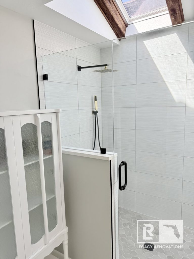 Modern walk-in shower with a wood-framed skylight, textured white wall tile, grey hex floor tiles, and matte black fixtures by Legacy Renovations in Jacksonville, FL.