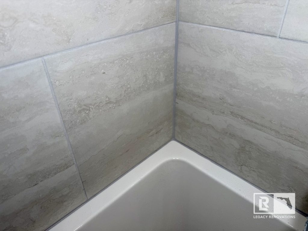 Close-up of a white bathtub and large-format gray porcelain tile corner during a bathroom remodel in Jacksonville, FL.