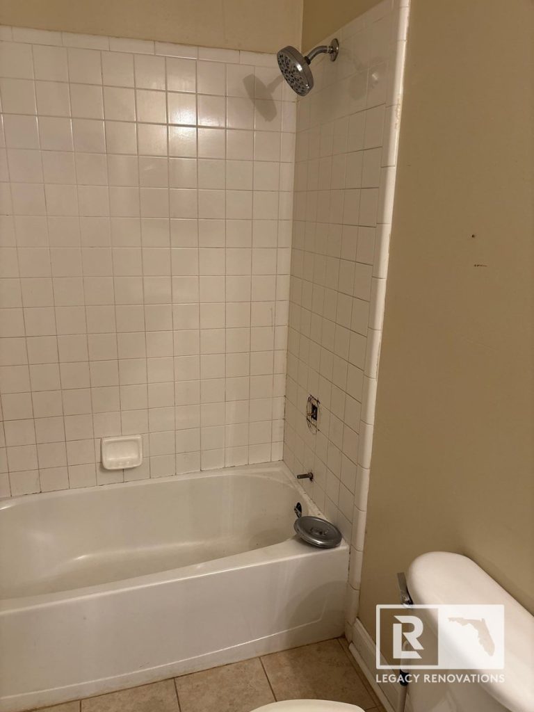 Before bathroom remodel showing an older white tile tub and shower surround prior to renovation in Jacksonville, FL.