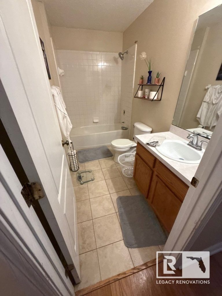 Before bathroom remodel featuring an outdated bathtub, white tile shower surround, wood vanity, and laminate countertop in Jacksonville, FL.