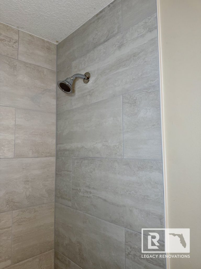 Walk-in shower with large-format gray porcelain tile walls and chrome showerhead during a bathroom remodel in Jacksonville, FL.