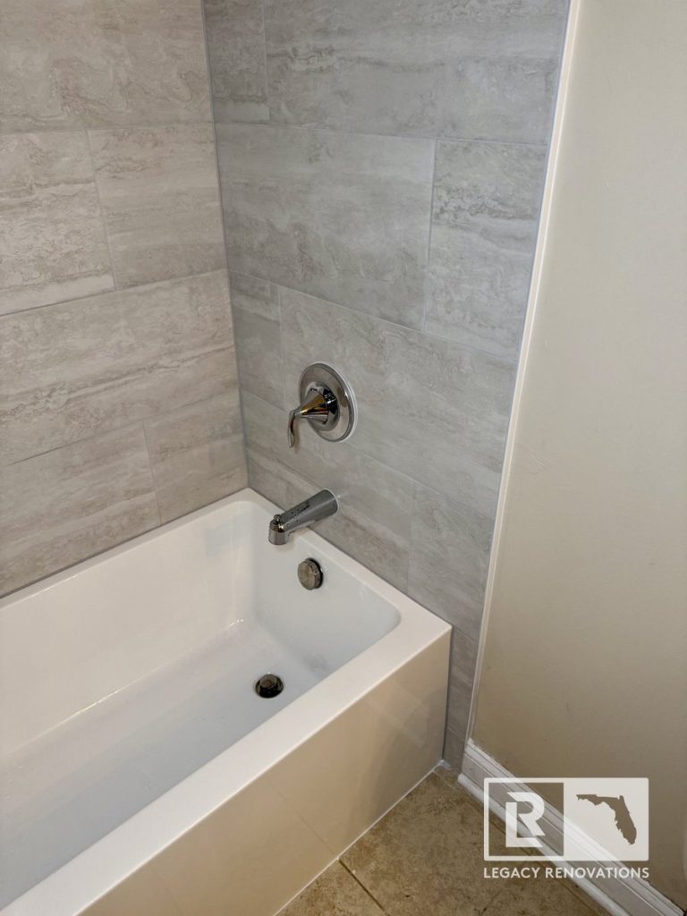 Gray porcelain tile bathtub surround with chrome shower fixtures in Jacksonville, FL bathroom remodel.