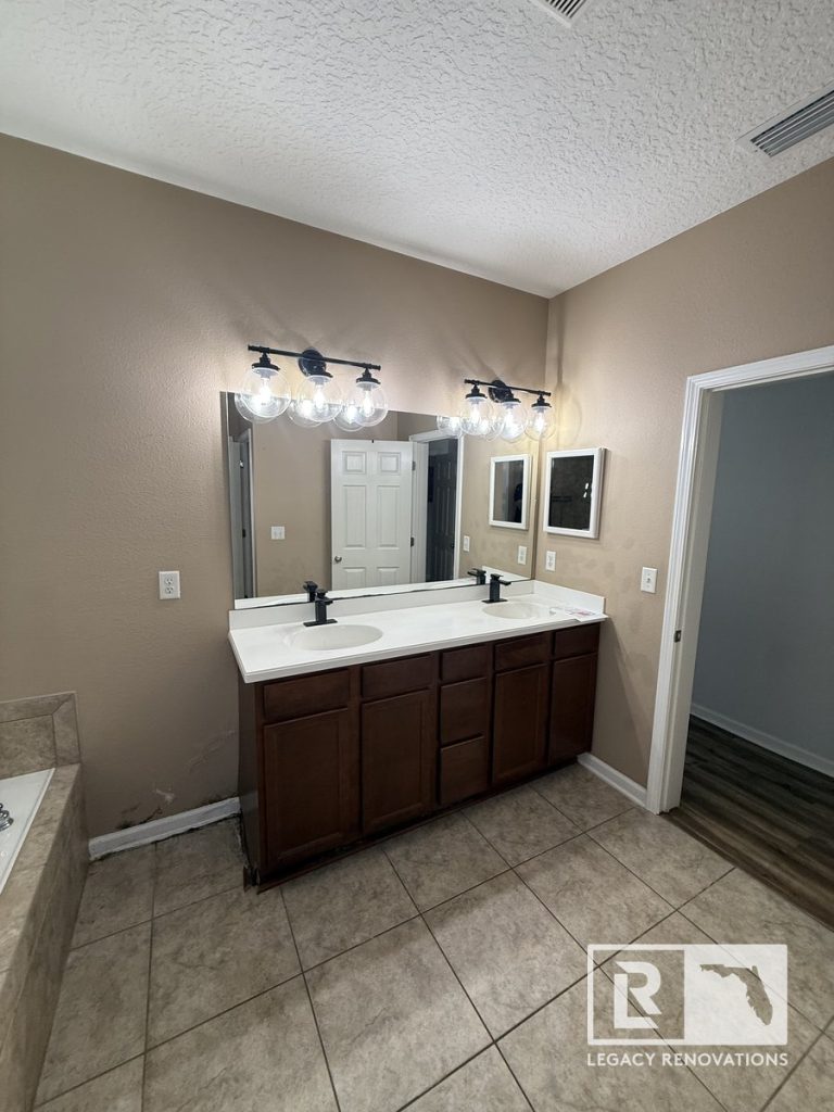 Original primary bathroom in Jacksonville, Florida before remodeling featuring an existing double vanity, wall-to-wall mirror, tile flooring, neutral wall colors, and the pre-renovation layout.