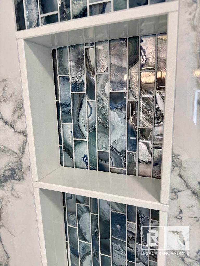 Angled close-up of a dual-compartment shower niche featuring blue agate mosaic tiles and white solid-surface shelving in Jacksonville, FL.